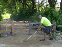 A grounds worker smooths the surface material on the path at the entrance to Picnic Point with a rake.