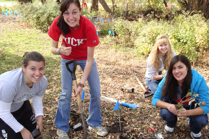 Four smiling student volunteers plant wildflowers along the Howard Temin Lakeshore Path.