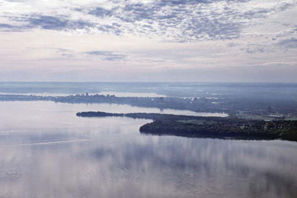 A pastel-colored sky is reflected in Lake Mendota in the foreground of this image featuring the dark outline of Frautschi Point, Picnic Point, and the Madison isthmus in an aerial view.