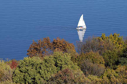 A sailboat on Lake Mendota near the wooded shoreline of the UW-Madison campus is pictured in an aerial view during autumn.